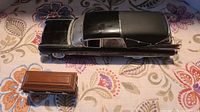 Top-down view of black 1959 Cadillac model hearse with wooden coffin accessory placed beside it