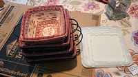 Stack of red cranberry pattern square ceramic dishes next to white plastic lids.