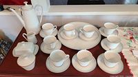 Full display of the vintage 29 piece Bavarian Schonwald white porcelain tea set on wooden table, showing teapot, cups, saucers, creamers, sugar bowl, and serving tray.