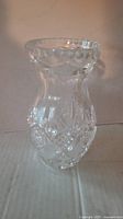 Clear crystal vase standing on a cardboard surface showing etched diamond and fan patterns, flared scalloped rim.