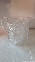 Front view of the vintage cut glass pitcher showing detailed starburst and diamond-cut patterns, scalloped rim and textured handle