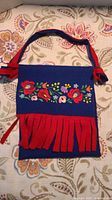Front view of vintage Hungarian purse showing colorful floral embroidery with a red felt strap and fringe.