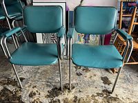 Front view of two green vinyl cushioned occasional chairs with tubular chrome frames and armrests.