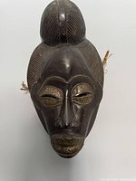 Front view of dark wooden African Punu mask showing calm expression with metallic accents around the eyes and mouth.