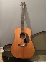 Full front view of guitar standing against wall showing dreadnought body and natural finish