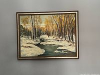 Framed oil painting showing winter scene with snowy banks, tall slender trees with autumn leaves, and a river flowing through the center.