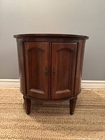 Front view of the round wooden side table showing two paneled doors with brass handles and tapered legs.