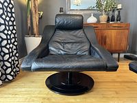 Front view of black leather swivel lounge chair on round base with mid-century modern sideboard in background