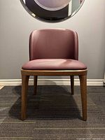 Front view of the maroon Mid Century Modern chair with wood legs against a wall with round mirror.