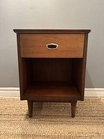 Front view of walnut nightstand showing drawer with metal pull handle and open shelf below.