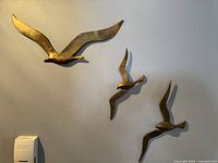 View of the full set of three brass seagull wall sculptures mounted on a light-colored wall, showing size differences and overall condition.
