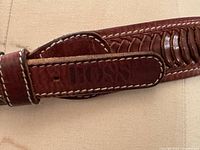 Close-up photo of the brown leather belt showing embossed 'BOSS' logo and detailed woven leather design with stitching