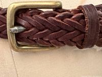 Close-up view of brass buckle and braided leather texture showing material quality and construction details.