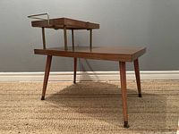 Side perspective of the wooden side table showing tapered legs and raised secondary tier attached with thin metal legs and supported with metal guard rail.