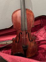 Close-up of the front face of the vintage violin inside the case, showing details of the body, strings, and fingerboard.
