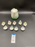 Full lot of nine small porcelain rose dishes and one porcelain cracker jar with lid, all displayed on a black surface.
