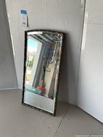 Full view of the rectangular vintage mirror leaning against a wall, showing the full frame and reflective surface.