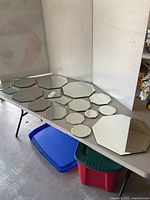 Display of fourteen assorted geometric mirrors laid on a table including octagonal, circular, hexagonal, and irregular shapes.