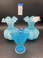 Pair of light blue Fenton 8-inch overlay glass vases with ruffled tops, standing behind a smaller deep blue opalescent hobnail fan vase.