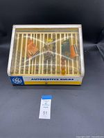 Closed view of the vintage G/E automotive bulb organizer showing the clear lid and yellow base with bulbs visible inside.