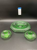 Three-piece set including one bowl and two candle holders made of green Depression glass with diamond pattern decoration.