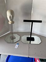 Two jewelry display stands on octagonal mirrored bases, one with mannequin head on clear pedestal, other with black T-bar necklace holder