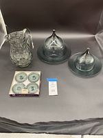 Full lot showing thumbprint glass pitcher, boxed set of 4 smoked glass candleholders, and two cheese domes with plates.