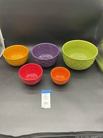 Five brightly colored stoneware nesting bowls displayed separately on a black surface.