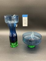 Photo showing the tall cobalt blue and green vase alongside the footed bowl, both placed on a black background with a small tag numbered 26.