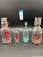 Four vintage milk bottles on a black background, including 2 Meadow Gold, 1 Anderson's Dairy, and 1 blue bottle.