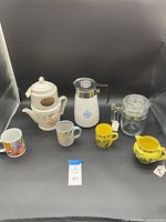 Photo showing all coffee makers and mugs in the lot arranged on a black background.