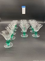 Front view of the 12 vintage etched Bird of Paradise glasses arranged in three rows, showing clear etched floral design and green square stems.
