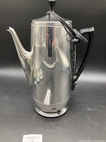 Full frontal photo of the vintage General Electric stainless steel coffee pot with lid and attached power cord.