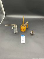 Photo showing three vintage oil cans on a black background with a lot tag labeled 48.