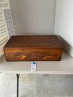Closed view of the wooden seed box showing the lid with faded printed design and signs of wear.