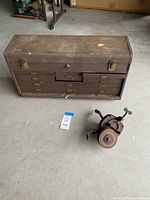 Vintage rusted metal tool box with multiple drawers sitting on concrete floor alongside a Niagara grinder.