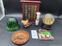 Photo of green glass twine holder, Givenchy snow globe, red vintage book box, Lucerne plaque, chef and turkey figurines, and a small colorful building decoration.