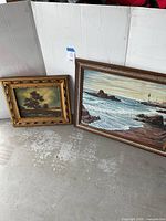 Two framed paintings placed on floor against a white wall, showing the lot contents.