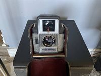 Front view of vintage Bell & Howell Electric Eye camera with lens and viewfinder, resting in an open leather or faux leather compartment base.