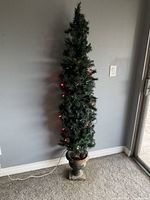 Front view of lit artificial faux tree inside a square decorative planter base against a wall.