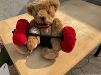 Steiff teddy bear in weightlifting outfit holding red barbell on wooden table in sunlight.
