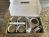Photo of the tea set items inside the box, showing teapot and four cups side by side with packaging separators