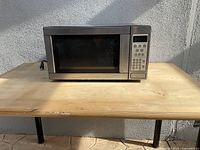 Large silver microwave oven on outdoor wooden table with door closed.