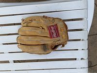Rawlings baseball glove placed palm side down on white slatted surface, tan color with red Rawlings patch and visible lacing