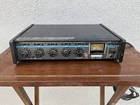 Front view of Shure M267 series microphone mixer placed on wooden table showing all control knobs, VU meter, input/output labels and power switch.