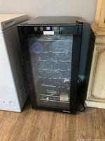 Black Vinotemp wine fridge from front, showing glass door, metal racks, and digital temperature display on top frame.