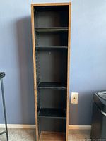 Photo showing the tall wooden storage case standing upright against a wall, with four shelves inside for storing DVDs, books, or cassettes.