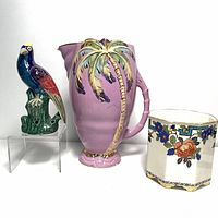 Photo showing colorful bird bud vase, purple jug with palm tree, and floral planter from front angle