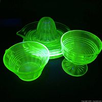 Five pieces of uranium and Depression glass under UV light showing bright green fluorescence.