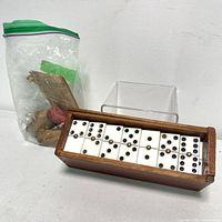 Domino tiles arranged in a wooden holder next to a plastic bag of game pieces.